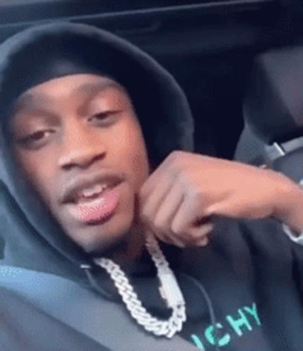 A Man Wearing A Hooded Sweatshirt And A Chain Around His Neck Is Sitting In A Car . GIF