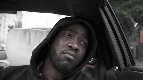 A Man Wearing A Hooded Sweatshirt Is Sitting In A Car GIF