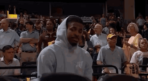 A Man Wearing A Hooded Sweatshirt Is Standing In Front Of A Crowd Of People At A Basketball Game . GIF