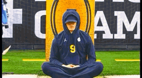 A Man Wearing A Hoodie Is Sitting In A Lotus Position On A Field . GIF