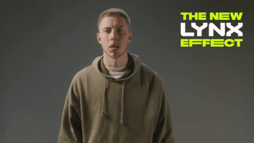 A Man Wearing A Hoodie Is Standing In Front Of A Sign That Says The New Lynx Effect GIF