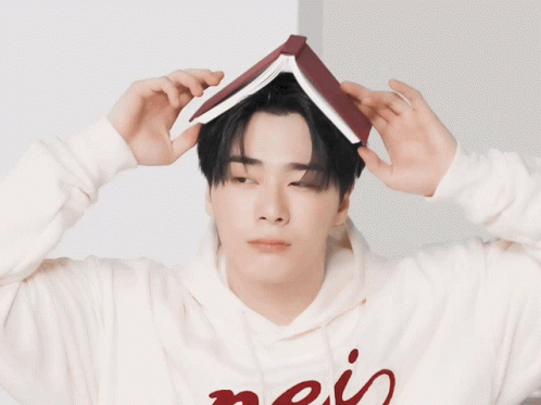 A Man Wearing A Hoodie With The Word Mais On It Holds A Book On His Head GIF