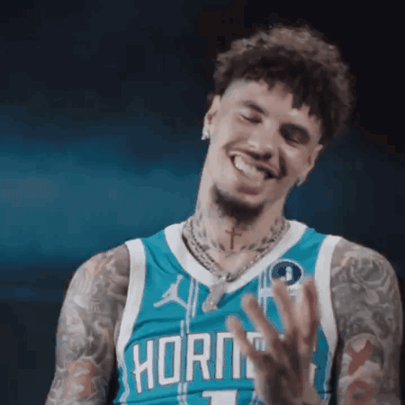 A Man Wearing A Hornets Jersey Is Smiling And Waving His Hand . GIF