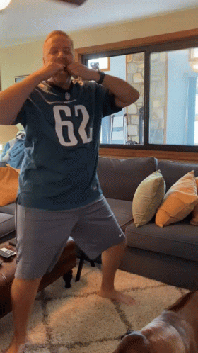 A Man Wearing A Jersey With The Number 62 On It Is Standing In A Living Room GIF
