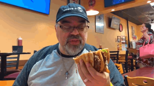 A Man Wearing A Jesus Hat Is Eating A Hamburger GIF