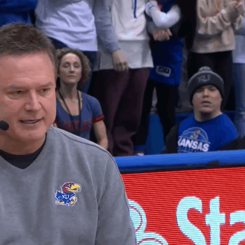 A Man Wearing A Kansas Shirt Is Sitting In Front Of A Crowd GIF