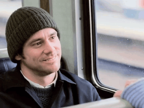 A Man Wearing A Knitted Hat Is Smiling While Sitting On A Train GIF