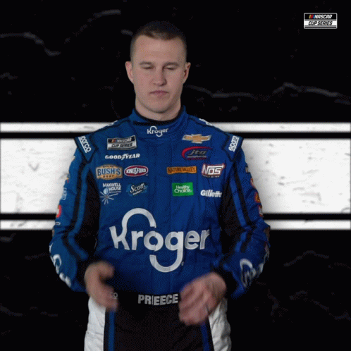 a man wearing a kroger racing suit stands with his eyes closed