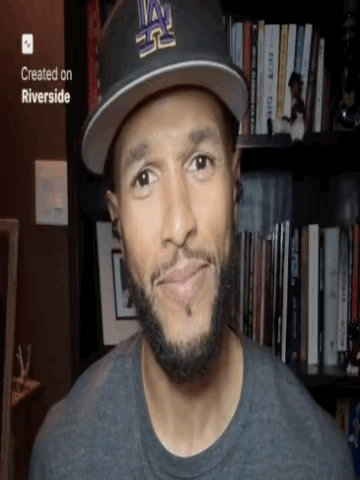 a man wearing a la hat is smiling in front of a bookshelf