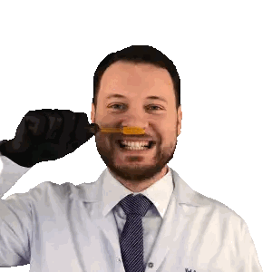 a man wearing a lab coat and tie is holding a yellow object in his mouth