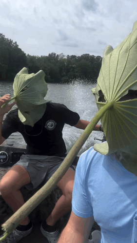 A Man Wearing A Leaf Mask Is Sitting On A Boat Next To Another Man GIF