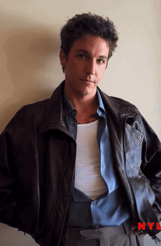 a man wearing a leather jacket and a blue shirt is standing in front of a nyl logo