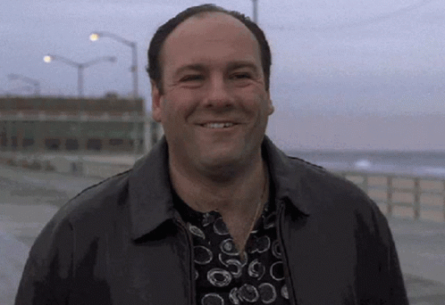 A Man Wearing A Leather Jacket And A Polka Dot Shirt Is Smiling On A Beach . GIF