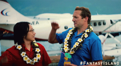 A Man Wearing A Lei Stands Next To A Woman Wearing A Lei And A Plane In The Background GIF