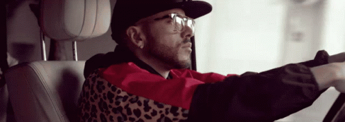 A Man Wearing A Leopard Print Jacket And Glasses Is Driving A Car GIF