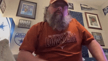 a man wearing a longhorns shirt is sitting in a room