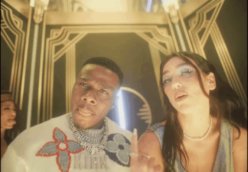 A Man Wearing A Louis Vuitton Sweater Stands Next To A Woman Wearing A Pearl Necklace GIF