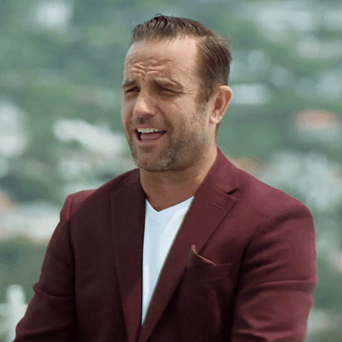 A Man Wearing A Maroon Jacket And A White Shirt Is Making A Funny Face GIF