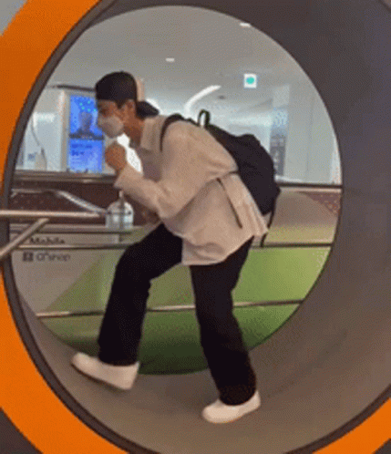 A Man Wearing A Mask And A Backpack Is Walking Through A Tunnel GIF