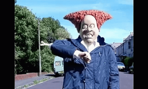 A Man Wearing A Mask And A Blue Jacket Is Giving A Thumbs Up While Standing On A Street . GIF