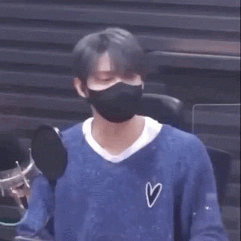A Man Wearing A Mask And A Blue Shirt Is Sitting In Front Of A Microphone . GIF