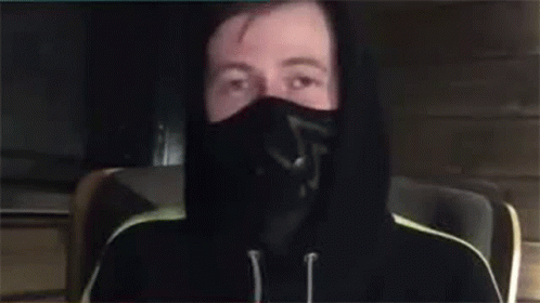 A Man Wearing A Mask And A Hoodie Is Waving His Hand . GIF
