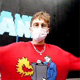 A Man Wearing A Mask And A Red Sweater With A Man Holding A Box GIF