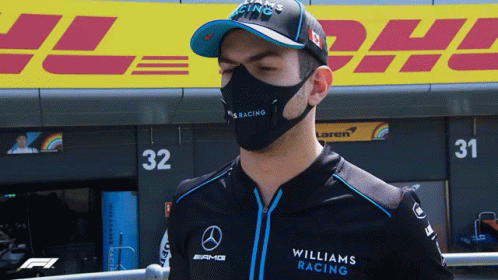 A Man Wearing A Mask And A Williams Racing Shirt Stands In Front Of Dhl GIF
