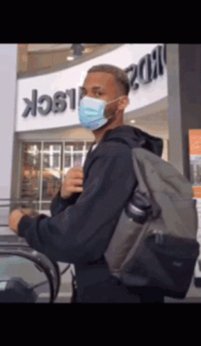 A Man Wearing A Mask And Carrying A Backpack Is Riding An Escalator GIF