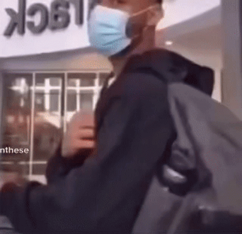 A Man Wearing A Mask And Carrying A Backpack Is Standing In Front Of A Sign That Says Lock GIF