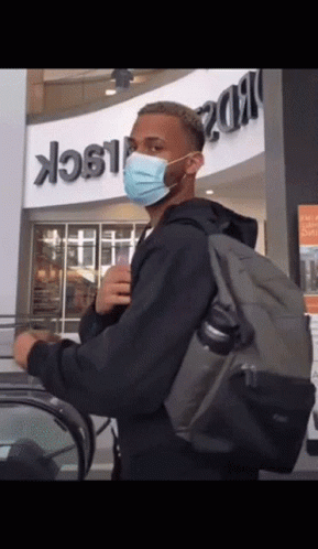 A Man Wearing A Mask And Carrying A Backpack Stands In Front Of A Building That Says Black GIF