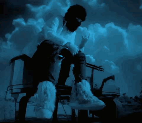 A Man Wearing A Mask And Furry Boots Is Sitting On A Chair GIF