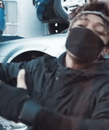 A Man Wearing A Mask And Gloves Is Sitting In Front Of A Car . GIF