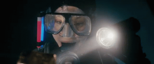 A Man Wearing A Mask And Goggles Is Holding A Flashlight In His Hand . GIF