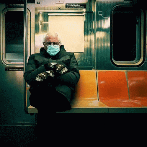 A Man Wearing A Mask And Mittens Sits On A Subway Train GIF