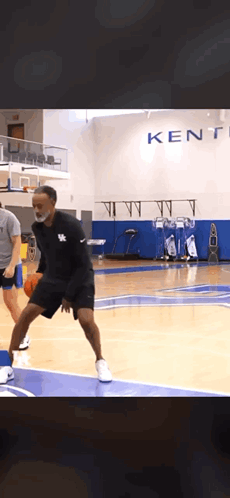 A Man Wearing A Mask Is Dribbling A Basketball On A Court In Front Of A Kentucky Sign GIF