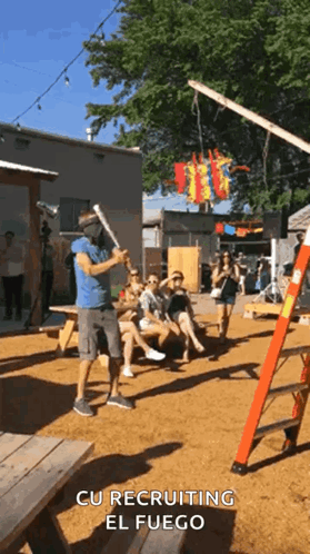A Man Wearing A Mask Is Holding A Bat In Front Of A Group Of People With The Words Cu Recruiting El Fuego Above Him GIF