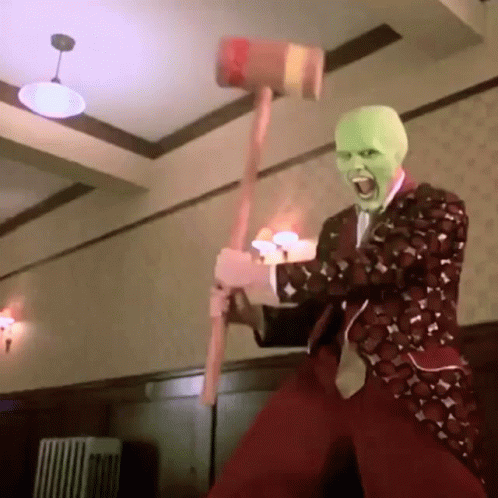 A Man Wearing A Mask Is Holding A Hammer In His Hand . GIF