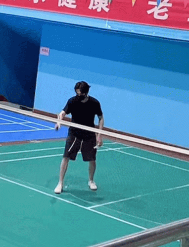 A Man Wearing A Mask Is Holding A Racket On A Badminton Court . GIF