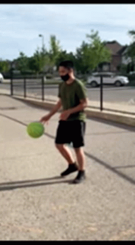 A Man Wearing A Mask Is Playing With A Ball On The Sidewalk GIF