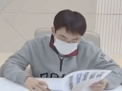 A Man Wearing A Mask Is Reading A Book . GIF