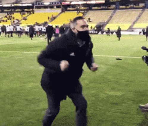 A Man Wearing A Mask Is Running On A Soccer Field . GIF
