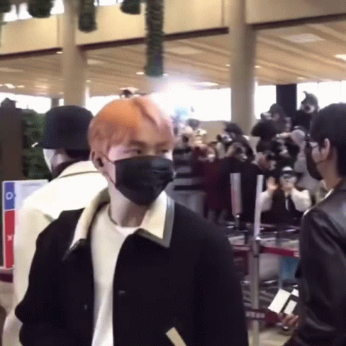A Man Wearing A Mask Is Standing In Front Of A Crowd Of People At An Airport . GIF