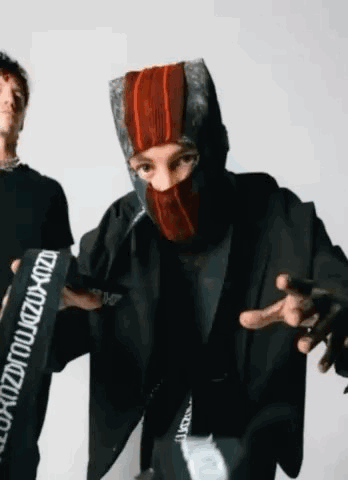 A Man Wearing A Mask Is Standing Next To Another Man Wearing A Jacket . GIF