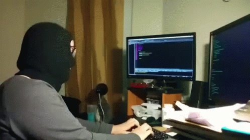 a man wearing a mask is typing on a keyboard in front of a computer monitor