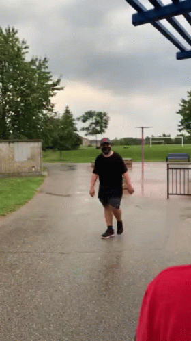 A Man Wearing A Mask Is Walking Down A Wet Street . GIF