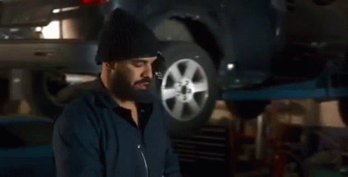 A Man Wearing A Mask Is Working On A Car On A Lift In A Garage . GIF