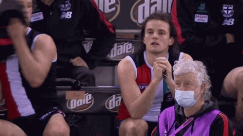 A Man Wearing A Mask Sits In A Stadium With A Sign That Says Date On It GIF