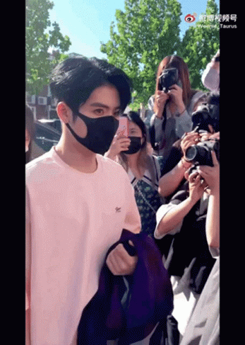 A Man Wearing A Mask Stands In Front Of A Crowd GIF