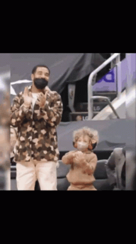 A Man Wearing A Mask Stands Next To A Young Boy Wearing A Mask GIF